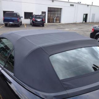 A close-up view of the soft top roof of a black convertible parked in a lot.