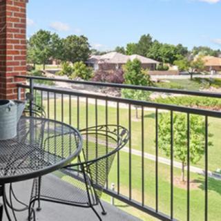 A scenic view from a balcony with a table and chairs overlooking a grassy area and houses.