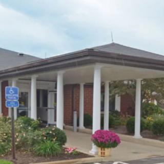 Entrance to a building with white columns, surrounded by well-maintained gardens and featuring accessible parking.