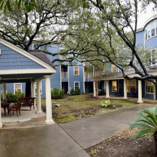A beautiful courtyard surrounded by a blue residential building with large trees and a covered porch area.
