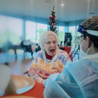 A joyful moment between an elderly woman and her caregiver during a holiday celebration.