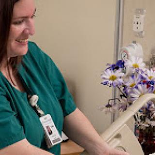 A smiling nurse providing care in a hospital environment with flowers in the background.
