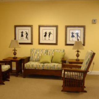 A cozy living room with a sofa, chairs, and artwork on a yellow wall.