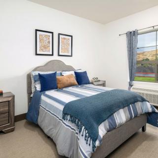A cozy bedroom with a neatly made bed, featuring blue and gray bedding, flanked by nightstands and adorned with artwork above the headboard.