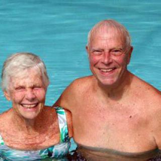 An elderly couple enjoying time together in a swimming pool, smiling happily.