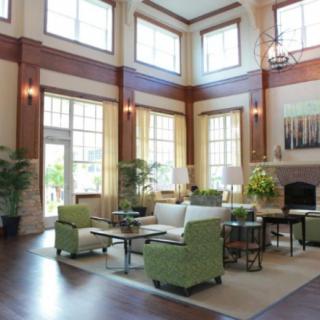 A spacious and modern living room with high ceilings and large windows, featuring comfortable green chairs and stylish decor.