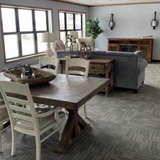 A cozy living room with a dining area, featuring rustic furniture and large windows.