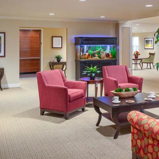 A cozy lobby area featuring two red armchairs, a coffee table, and a fish tank in the background.