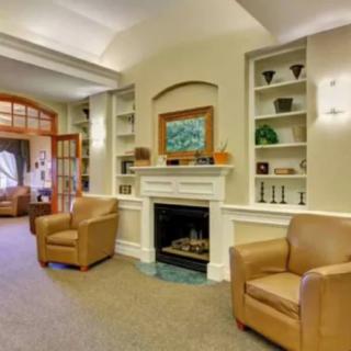 A cozy living room featuring a fireplace, armchairs, and neatly arranged shelves.