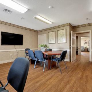 A well-lit conference room featuring a large table surrounded by chairs, a wall-mounted television, and wooden flooring.