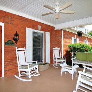 A cozy porch with white rocking chairs and a ceiling fan, surrounded by a red brick wall and greenery.