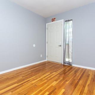 An empty room with a hardwood floor and a white door adorned with curtains.