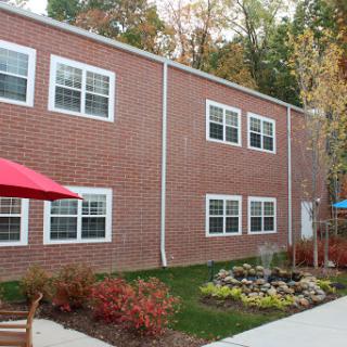 A brick building featuring multiple windows, set in a landscaped area with outdoor seating.
