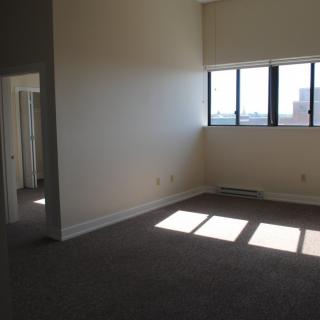 An empty apartment room with large windows allowing sunlight to stream in.