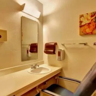 A small bathroom with a sink, mirror, and towel dispenser.