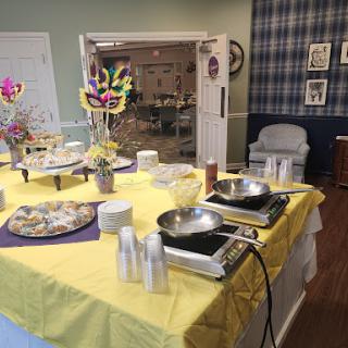A buffet setup with a yellow tablecloth, featuring various food items and kitchenware in a decorated event space.
