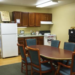 Office kitchen with a round table and chairs, equipped with a refrigerator and stove.