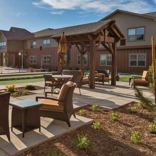 A well-maintained outdoor patio area with comfortable seating and a landscaped garden, set against the backdrop of a modern building on a sunny day.