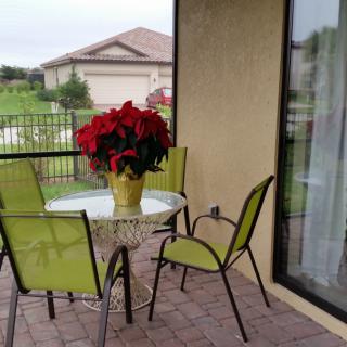 A cozy patio setup with green chairs and a table adorned with a potted plant featuring vibrant red flowers.