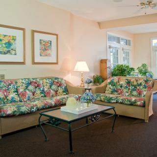 A cozy living room featuring floral-patterned sofas, a glass-topped coffee table, and decorative artwork on the walls.
