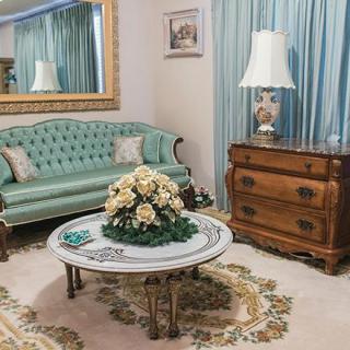 A vintage-style living room with a green tufted sofa, ornate coffee table adorned with flowers, and classic wooden furniture.