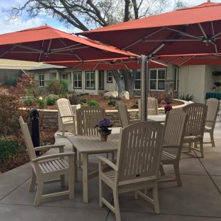 A cozy outdoor patio with tables, chairs, and red umbrellas providing shade in a garden setting.