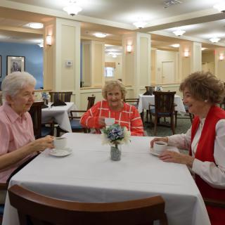 Three senior women enjoy a meal together, engaging in conversation at a dining facility.