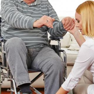 A caregiver assists an elderly man in a wheelchair indoors.