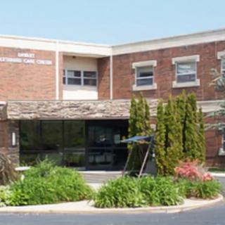 A brick building with an entrance surrounded by plants and trees, resembling a school.