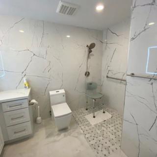 A modern bathroom with marble tiles, featuring a toilet, sink, and walk-in shower.