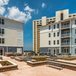 A modern residential apartment complex with outdoor seating and balconies under a bright blue sky.