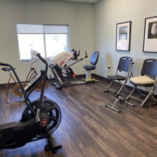 A small gym with exercise bikes and chairs on a wooden floor.