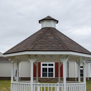 A charming wooden gazebo with a conical roof, set against a backdrop of cloudy skies.