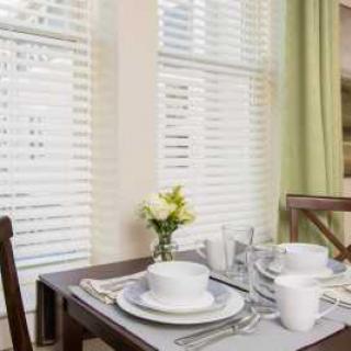 A neatly set dining table with white dinnerware, glasses, and a small vase of flowers by the window.