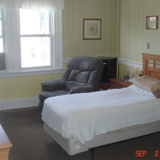 A cozy bedroom with a single bed, armchair, and large window.
