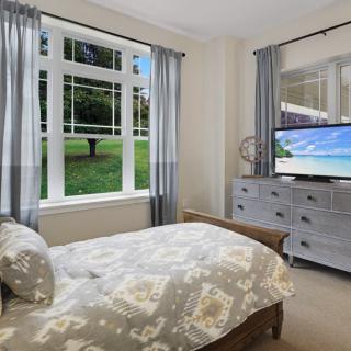 A cozy bedroom with a large window, curtains, and a television on a dresser.