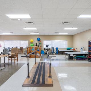 A spacious physical therapy room equipped with parallel bars and various exercise tools for rehabilitation exercises.