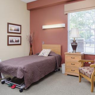A cozy bedroom featuring a single bed, nightstand with a lamp, and warm-toned walls.