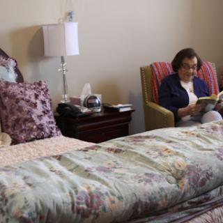 A cozy bedroom scene featuring a person reading in an armchair next to a neatly made bed.