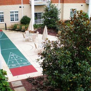 A courtyard featuring a shuffleboard court surrounded by greenery and seating areas.