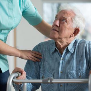 A caregiver assisting an elderly man using a walker.