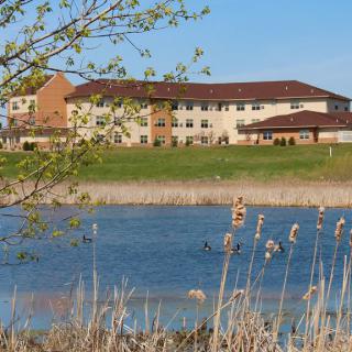 A building by a lake with surrounding nature and clear skies.
