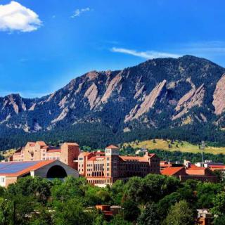 A scenic view of a city nestled at the base of majestic mountains under a clear blue sky.