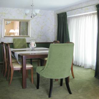 A cozy dining room with a table and green upholstered chairs, complemented by a mirror on the wall and elegant curtains.