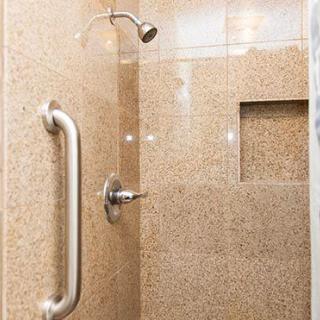A tiled shower with a grab bar and a recessed niche.