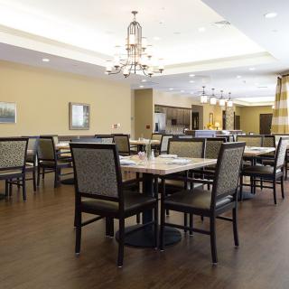 A well-lit dining room with neatly arranged tables and chairs, featuring elegant chandeliers.