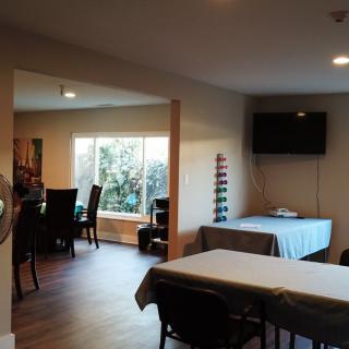 A cozy dining area with tables, chairs, a TV, and natural light streaming through a large window.