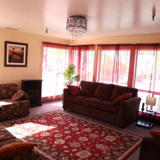 A cozy living room with a large sofa, armchair, and decorative rug, illuminated by natural light from the windows.