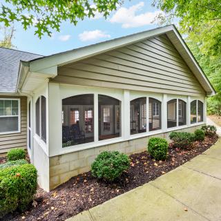 A charming house with a screened porch surrounded by well-maintained landscaping.