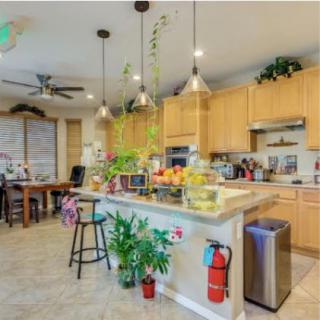 A modern kitchen with wooden cabinets, pendant lighting, and a central island adorned with plants and fruit baskets.